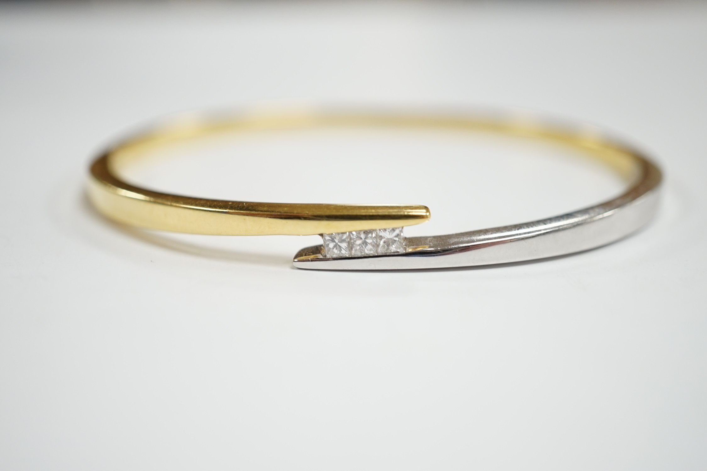 A modern two colour 18k and three stone princess cut diamond set hinged bangle, interior 60mm, gross weight 23.4 grams.